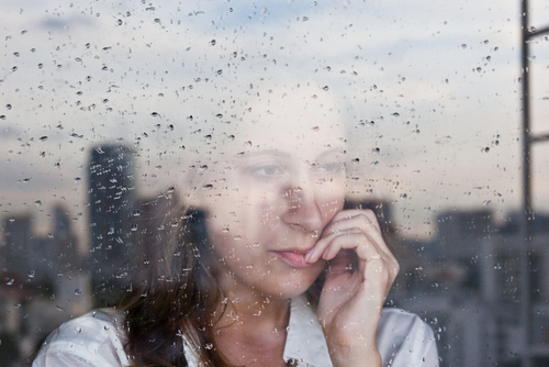 A woman stares out a rainy window.